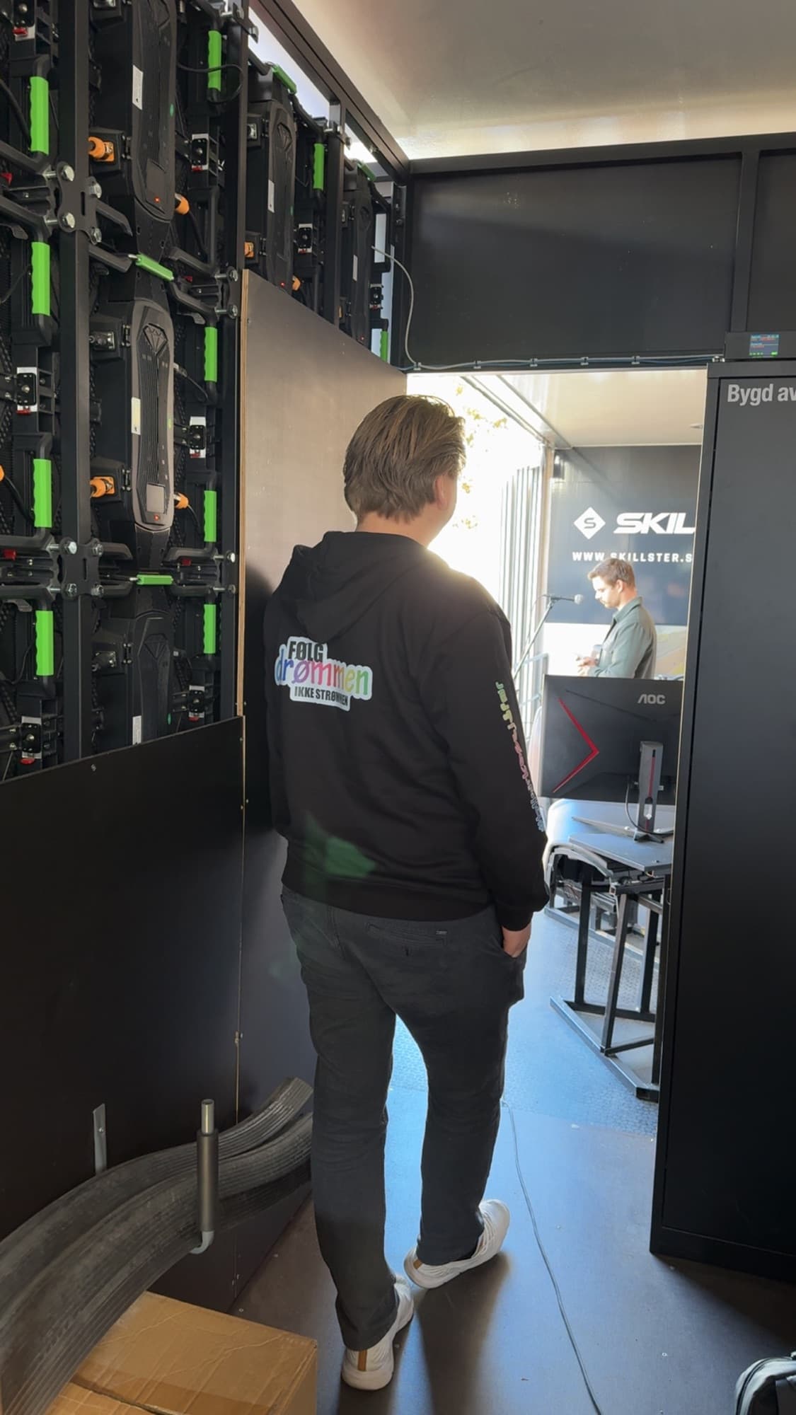 Ung mann i Følg drømmen-genser inne i traileren, med skjermvegg og simulatorer rundt seg