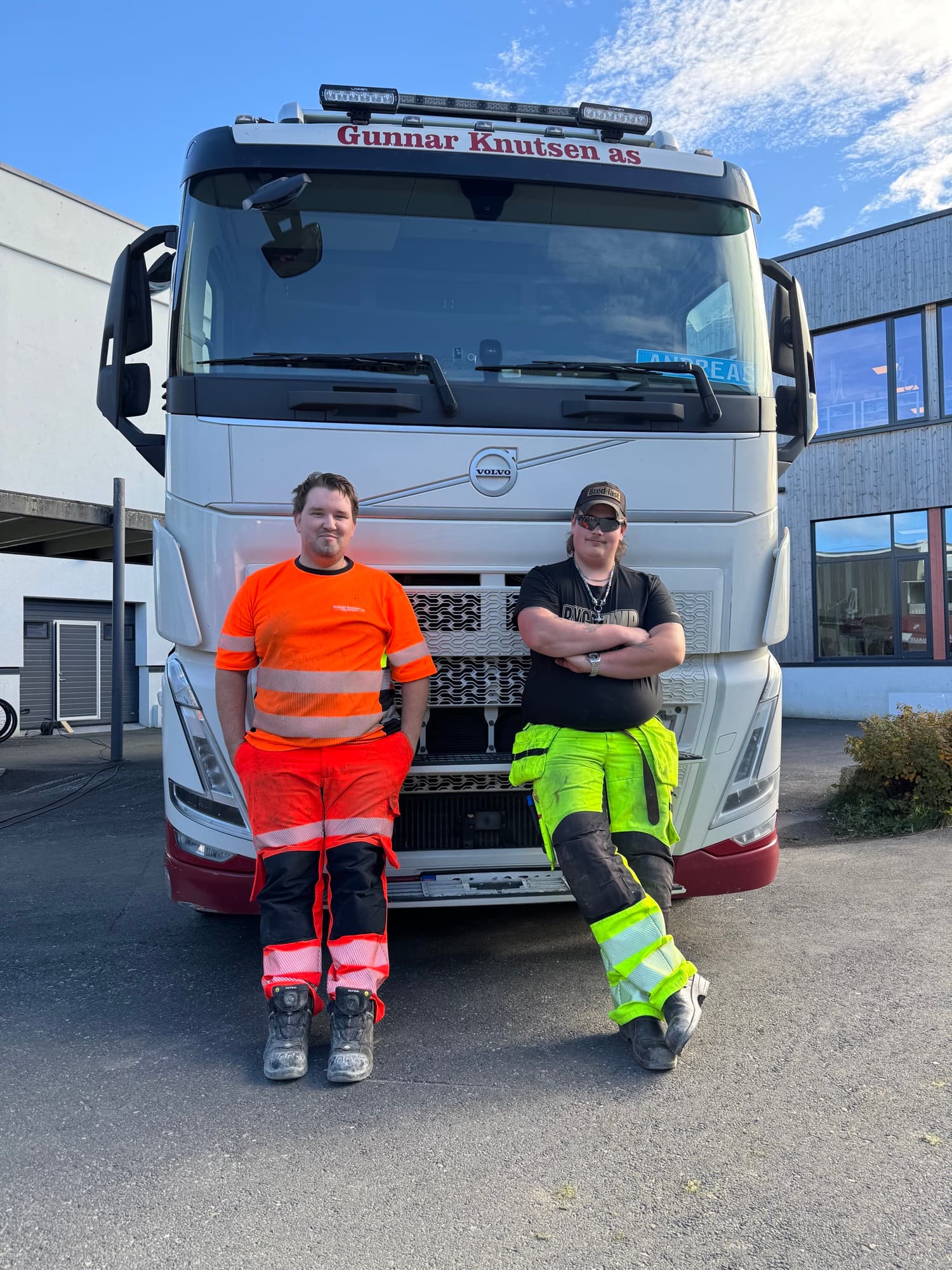 To unge menn i arbeidsklær lener seg mot fronten av en hvit Volvo-lastebil fra Gunnar Knutsen AS